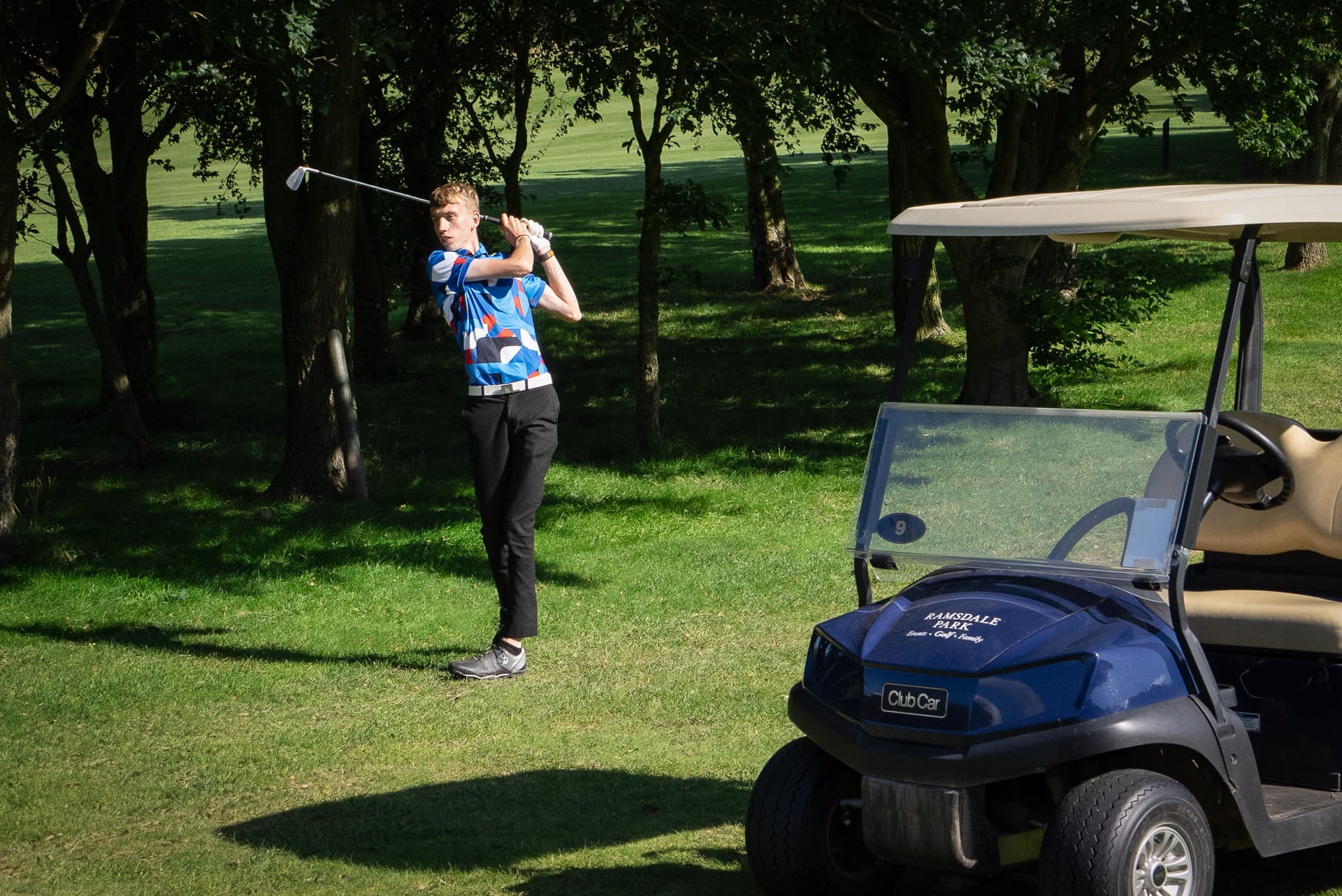 Golfer swinging club by a golf buggy